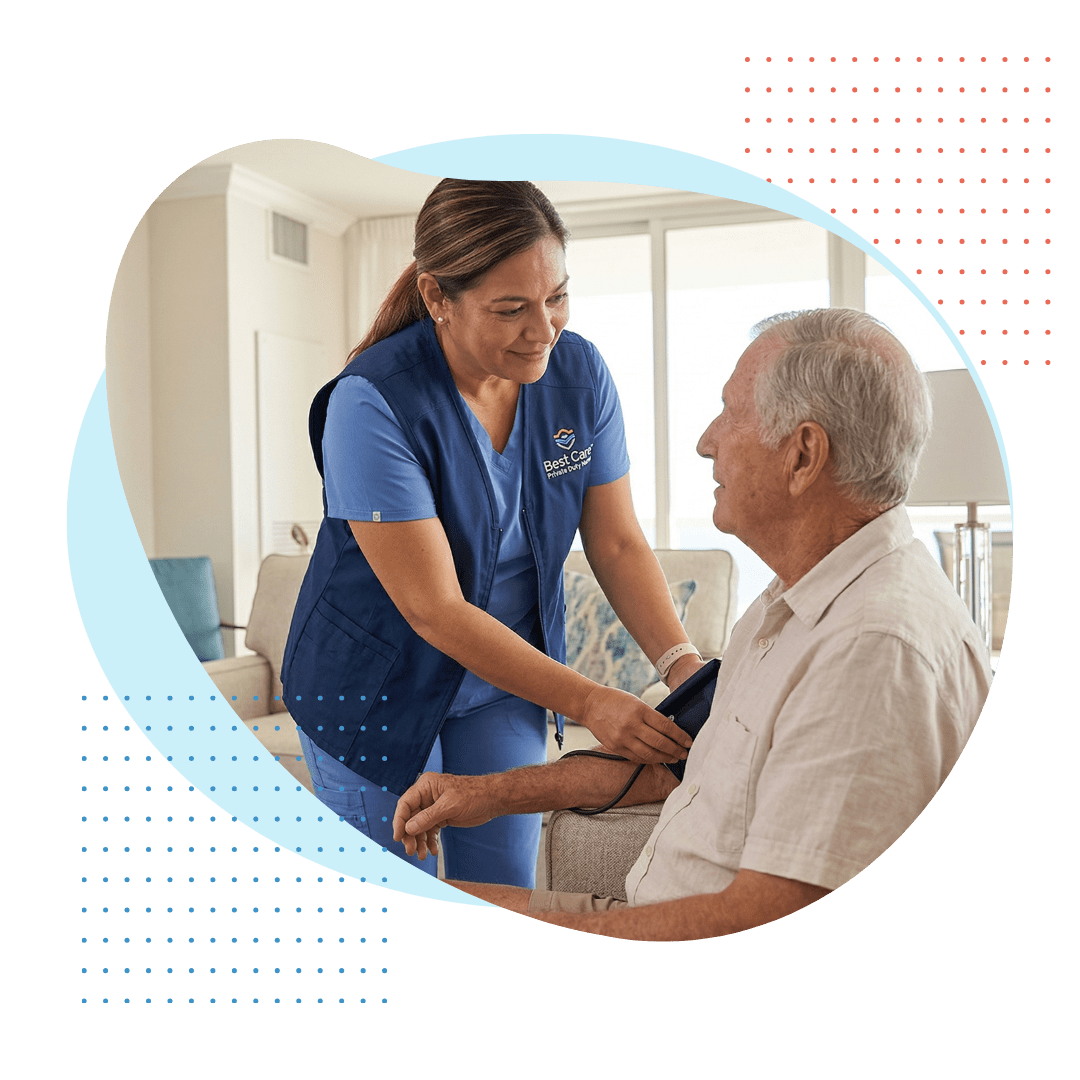 A compassionate female Best Care private duty nurse, wearing clean blue scrubs with a branded vest, is carefully checking the vitals of a seated senior man with natural daylight highlighting the detailed, gentle interaction.
